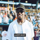 Jerry Jeudy smiling at a baseball game wearing a white jersey, black cap, and LosReyes polarized black sports sunglasses.