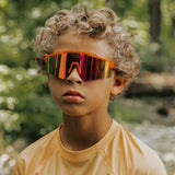 Youth lifestyle image of LosReyes Prime Jurassic Triceratops sunglasses in vibrant orange with a mirrored shield lens and wraparound sport frame, designed for outdoor performance, active wear, and full UV protection.