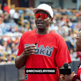 Michael Irvin speaking into a microphone at a celebrity game event, wearing LosReyes polarized red sunglasses.