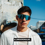 Urban lifestyle photo of @erickronaldo wearing LosReyes blue mirrored shield sunglasses, styled with a crisp white jacket against a city backdrop—merging high-performance eyewear with modern street fashion