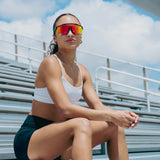 Lifestyle photo of athlete wearing LosReyes Prime Polarized Red mirrored sunglasses on track bleachers, highlighting red reflective lens, tactical matte frame, and competition-ready look for elite sport and sun protection.