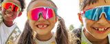 Smiling kids close-up outdoors on the playground, wearing colorful LosReyes mirrored sports premium glasses in pink, red, and blue, fun cool summer basketball-inspired children’s eyewear with uv protection