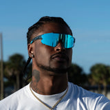 Man wearing LosReyes elevate blue raz wraparound sunglasses with braided hair and white T-shirt, posing outdoors under a clear sky – premium men’s performance eyewear