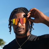 Man adjusting LosReyes Elevate Peach wraparound sunglasses while wearing black shirt and gold necklace – bold performance sunglasses for outdoor style.