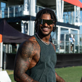 Ross500 wearing Elevate Marshmallow LosReyes sunglasses with muscle tank top and tattoos, standing on a sunny sports field – men’s luxury wraparound sunglasses with UV protection.