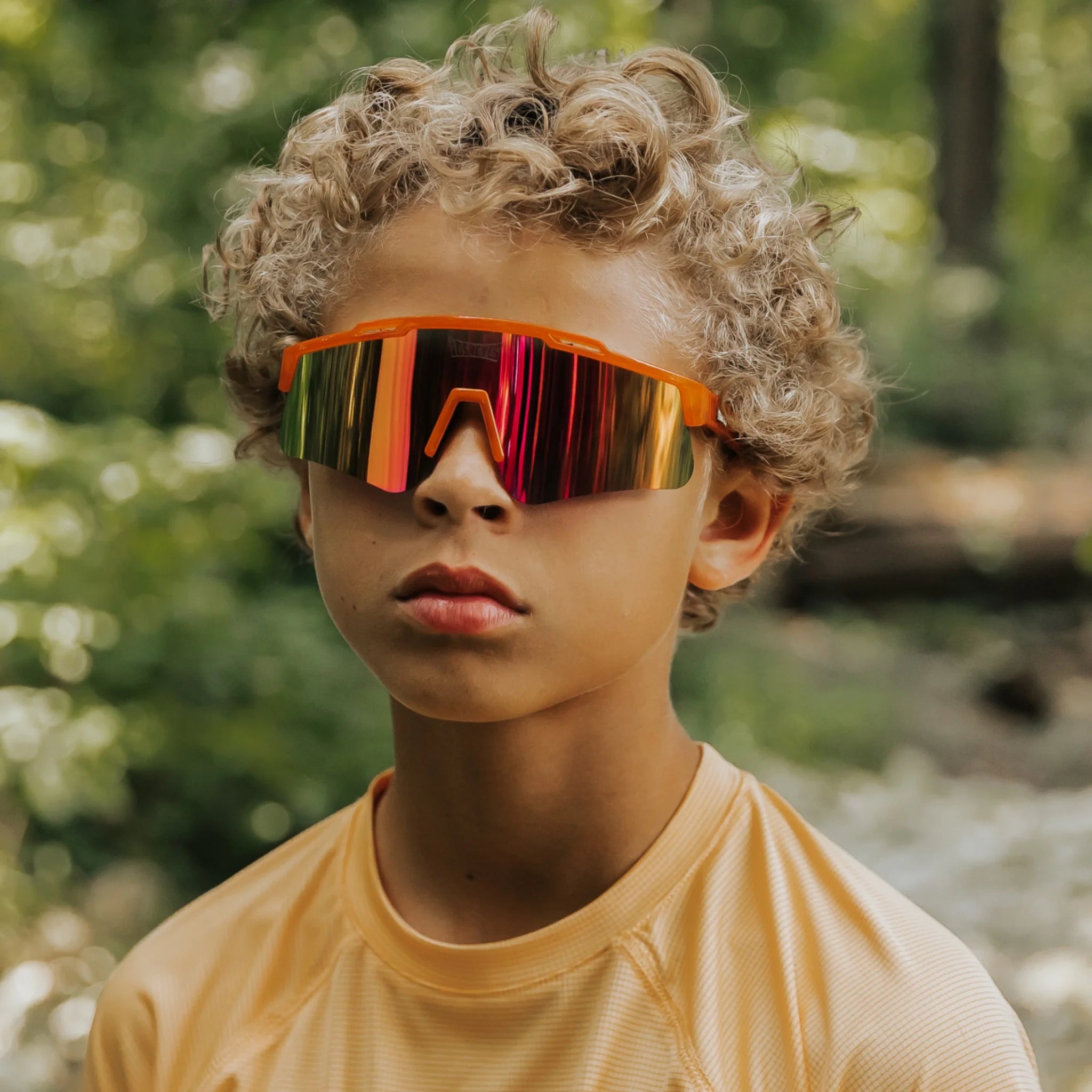 Youth lifestyle image of LosReyes Prime Jurassic Triceratops sunglasses in vibrant orange with a mirrored shield lens and wraparound sport frame, designed for outdoor performance, active wear, and full UV protection.