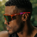 Side profile lifestyle photo of LosReyes Prime Jurassic Triceratops sunglasses in orange and red with a mirrored shield lens and aerodynamic wraparound frame, designed for outdoor athletic use and bold UV400 protection.