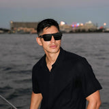 The LosReyes Hades sunglasses featured in a nighttime waterfront scene. Dark smoked lenses and stealth-black frame engineered for bold nighttime style.