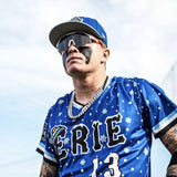 Max Clark looking up in an Erie Seawolves Christmas-themed blue jersey, sporting LosReyes SHOWTIME sunglasses with black face-paint strips down his cheeks.