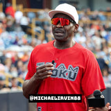 Michael Irvin speaking into a microphone at a celebrity game event, wearing LosReyes polarized red sunglasses.