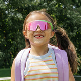 Smiling child wearing Candy Collection Sour Apple pink and green kids sport sunglasses outdoors