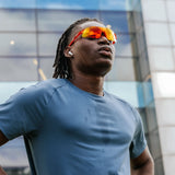 Model wearing Edge Lava sunglasses during outdoor activity, featuring red-orange mirrored shield lenses.