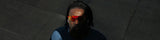 Person wearing reflective red performance edge lava sunglasses from LosReyes in dramatic shadow lighting, viewed from above against a dark textured background.