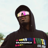 Lifestyle photo of AJ Greene wearing LosReyes iridescent mirrored shield sunglasses styled with a black hoodie, combining high-performance athletic eyewear with streetwear fashion and urban edge