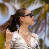 Woman wearing black LosReyes lifestyle sunglasses under palm trees, featuring sleek UV400 lenses and modern TR90 frame design inspired by Miami streetwear.