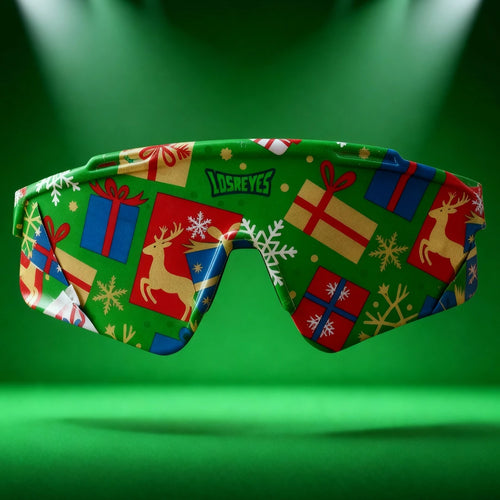 LosReyes sunglasses wrapped in festive Christmas gift paper with reindeer and snowflake patterns, displayed under spotlight on a green background — premium holiday eyewear.