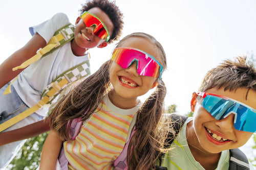 Kids wearing LosReyes sunglasses with colorful lenses and backpacks, smiling outdoors