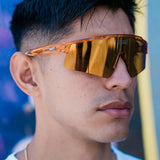 Lifestyle front view of LosReyes Prime Galaxy Jupiter performance sunglasses in orange with gold mirrored lenses, styled for streetwear-meets-sport appeal.