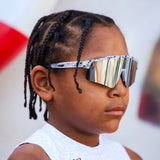 Close-up side view of LosReyes Prime Youth Cookie sunglasses on kid with braids, featuring reflective shield lens, lightweight temples, and sporty black speckle frame.