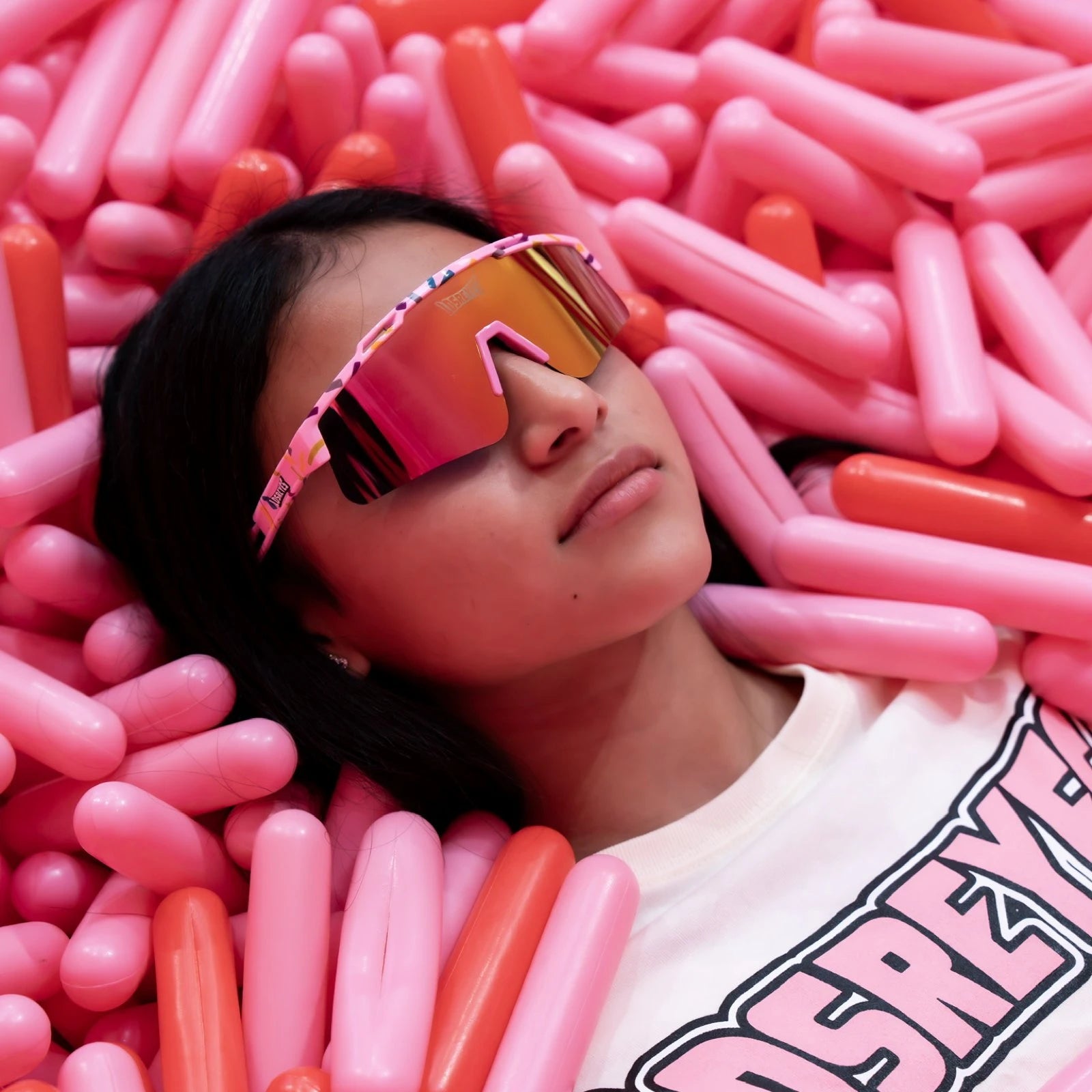 Creative lifestyle photo of girl in pink ball pit wearing LosReyes Prime Youth Cream kids wraparound sunglasses with mirrored pink lenses and UV400 protection