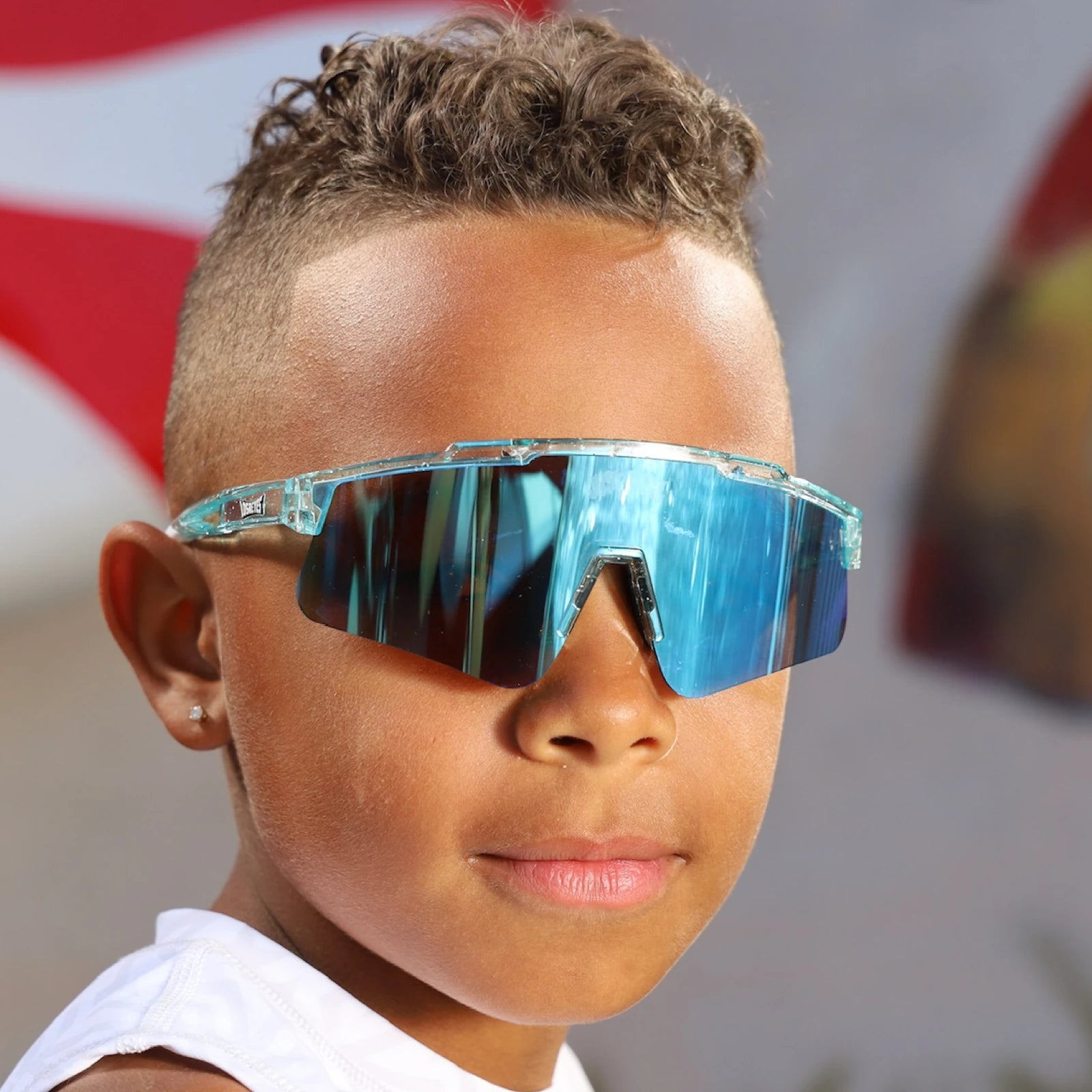 Front angle of LosReyes Prime Youth Ice Cube sunglasses on young boy, highlighting cool blue iridium wraparound lenses, frosted transparent frame, and sport-performance fit with UV400 lens technology.