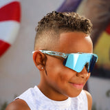 Side view of LosReyes Prime Youth Ice Cube sports sunglasses worn by kid, showcasing blue mirrored shield lenses, white ear grips, and icy translucent frame, designed for active youth and full UV400 protection.