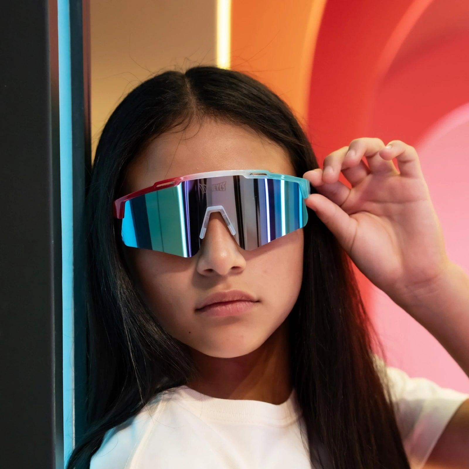 Portrait lifestyle shot of girl wearing LosReyes Prime Youth Rocket Pop mirrored sports sunglasses in red, white, and blue with reflective blue lens and UV400 protection. Designed for active youth style and everyday athletic performance.