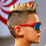 Side profile of LosReyes Prime Youth Rocket Pop wraparound sunglasses for kids with patriotic red and blue frame, blue iridium lens, and UV400 protection. Performance-ready shield eyewear for youth athletes and outdoor play.