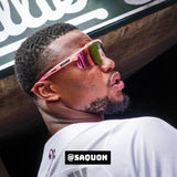 Side-angle lifestyle photo of Saquon Barkley wearing LosReyes pink mirrored shield sunglasses with a wraparound athletic frame, styled during a pro baseball event