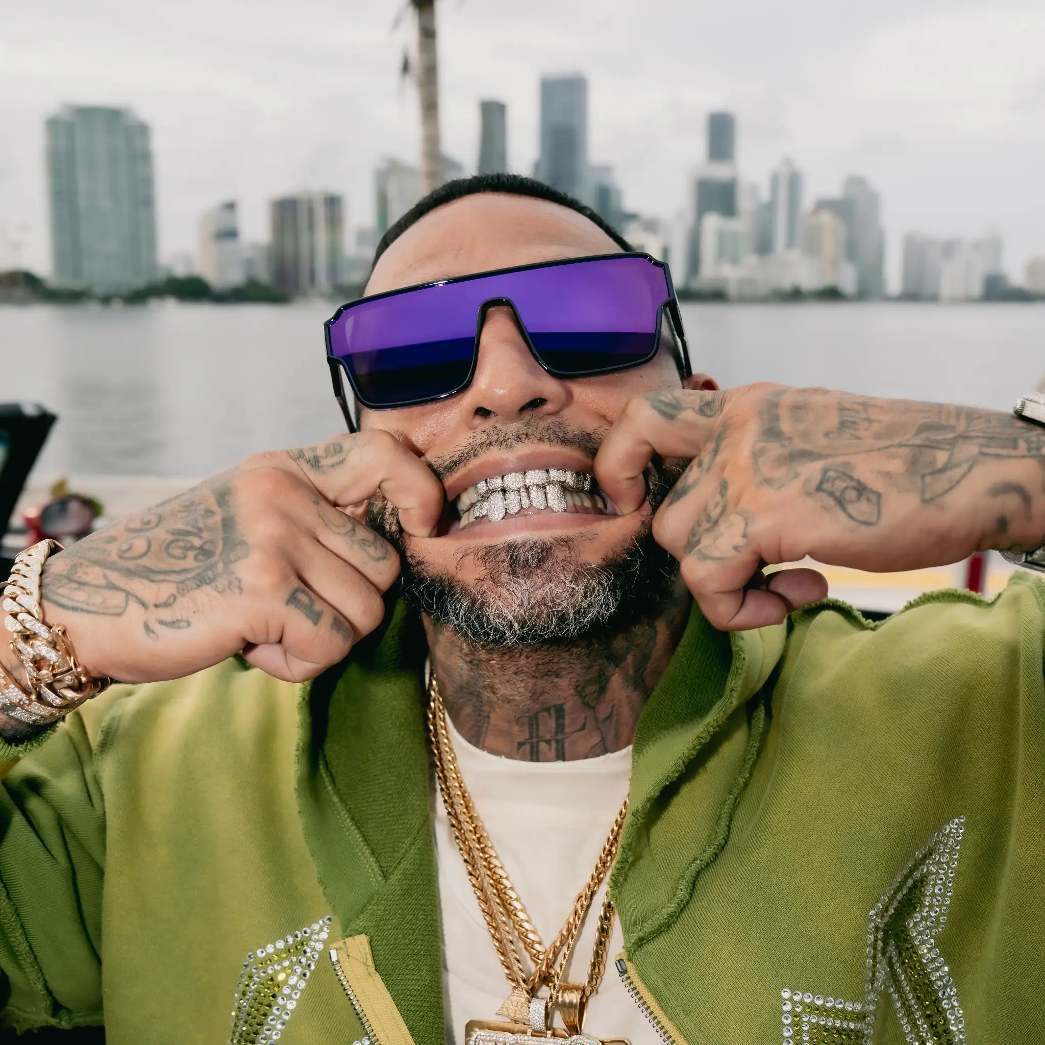 Man wearing LosReyes Zeus sunglasses and a green jacket with a city skyline in the background